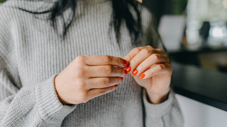 Close-up of feminine figure in a grey schedule, touching her red, gel manicured nails