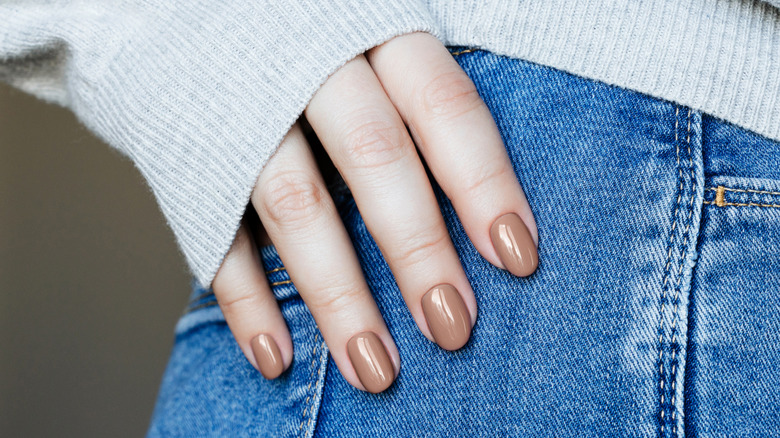 Close-up of feminine hand with shiny brown nail polish against denim jeans