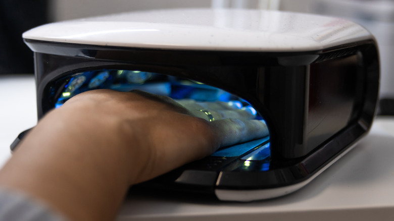 A feminine hand resting within a UV curing device