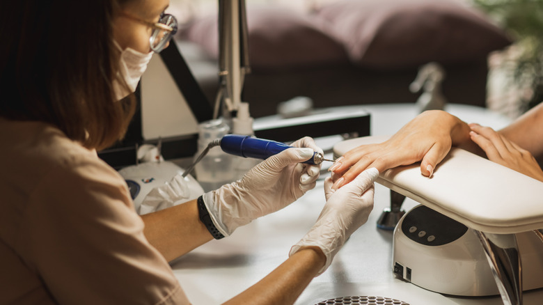 Unseen woman with finished nails receiving nail care from technician