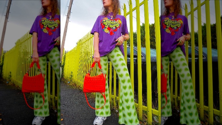 Person posing in vibrant outfit by yellow fence