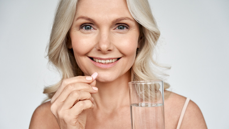 Woman holding vitamin glass of water smiling