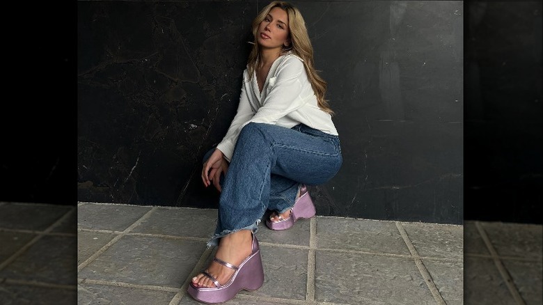 Woman in jeans, white shirt, and pink sandals posing