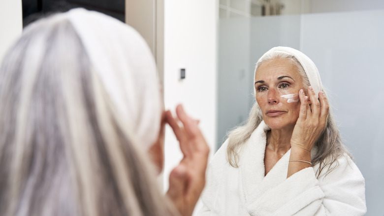 Mature woman looking into a mirror and applying face cream