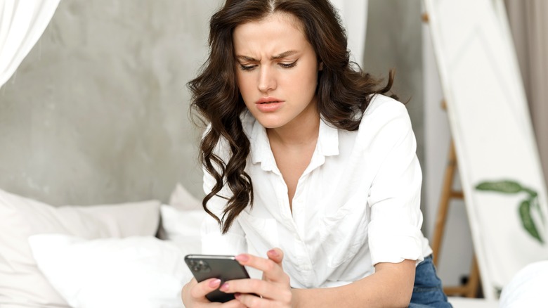 A woman frowns, looking at her phone