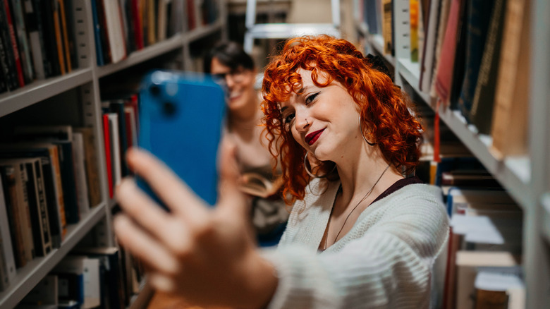 Redheaded woman taking a picture with a friend among bookshelves