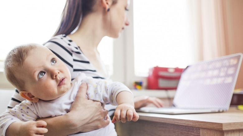Woman holding baby while working at laptop
