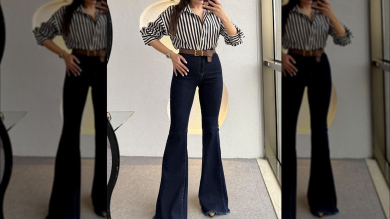 A woman taking a selfie in the mirror wearing dark wash flared jeans and a striped shirt