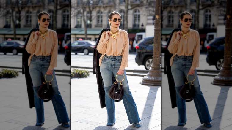 A woman wearing flared jeans and a pale pink blouse