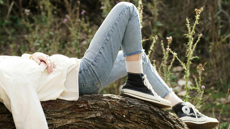 a woman in a white shirt, skinny jeans, and converse laying on a log outdoors