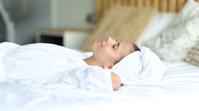 Woman with white towel around hair laying in bed. 