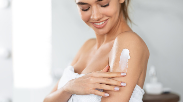 Woman wrapped in towel applying lotion to bare arms
