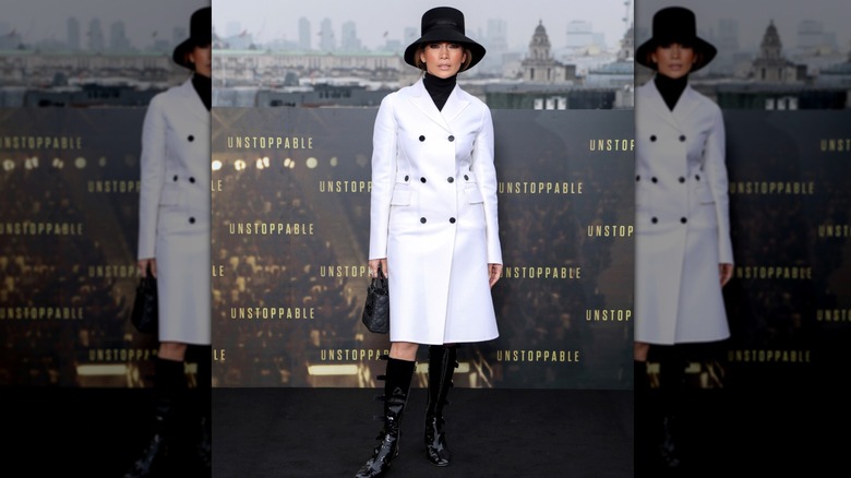 Jennifer Lopez in London wearing a white double breasted coat, patent leather boots, and black hat