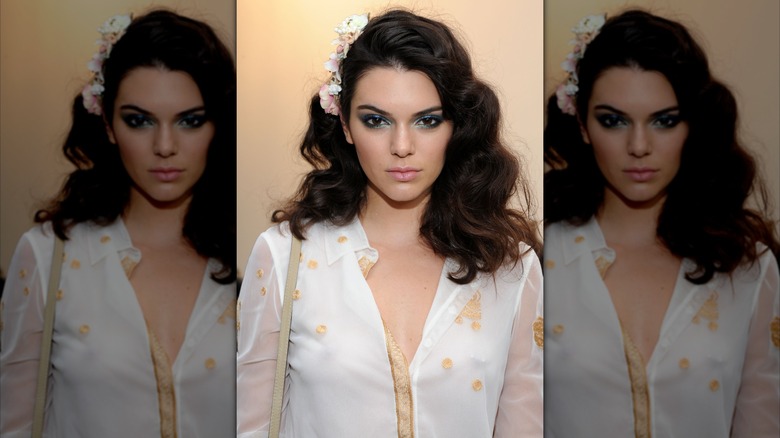 Kendall Jenner posing against a beige wall with textured, wavy hair