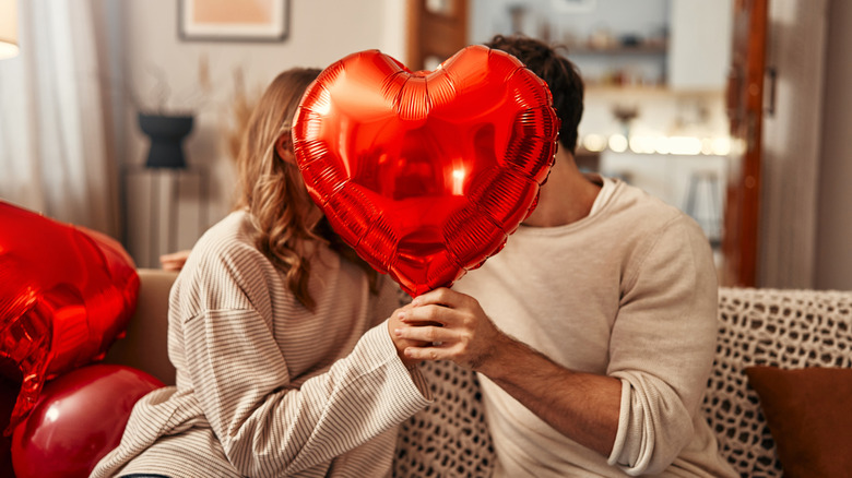 two people kissing behind a red heart-shaped balloon