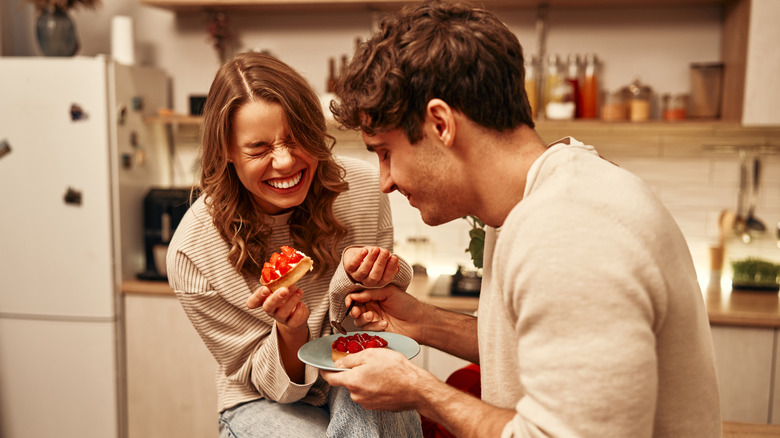 Couple laughing with fruit tarts in the kitchen