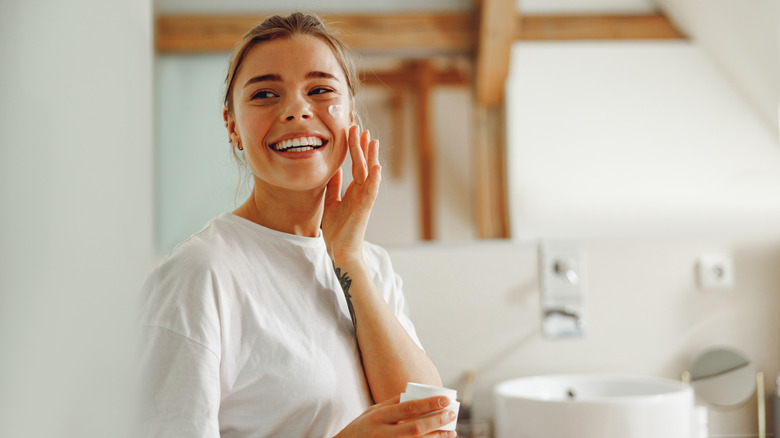 A young woman smiling and applying face cream