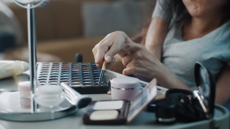 Disabled woman holding makeup brush to apply makeup from palettes on a table