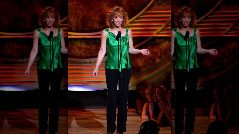 Reba McEntire standing in front of a microphone while wearing a silk green top