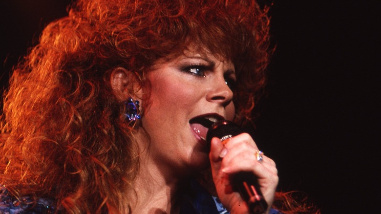 Reba McEntire singing into a microphone wearing heavy makeup