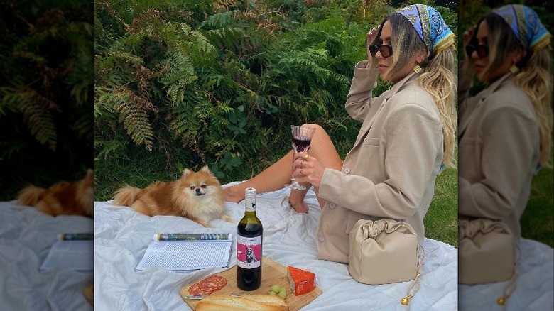 Woman with glass of wine on picnic blanket with dog