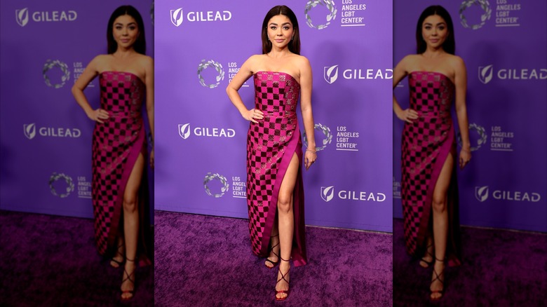 Sarah Hyland posing with her hand on her hip in a checkered, pink dress