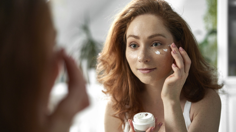 Woman looking in mirror and applying sunscreen