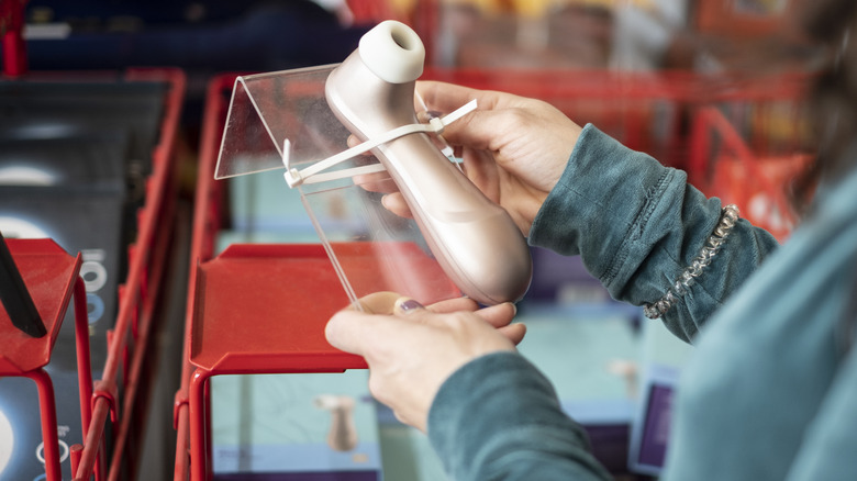 Woman holding a Satisfyer clitoral stimulator at an adult toy store