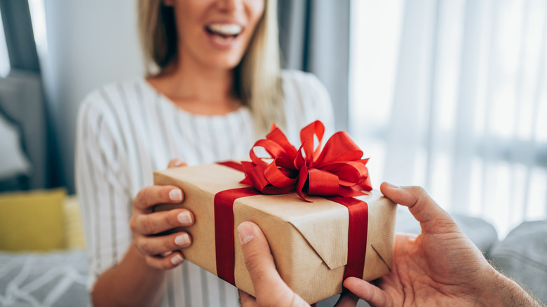 A man's hands passing a woman in a white sweater a box with a red ribbon