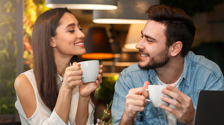 Couple on a date, both smiling, holding mugs