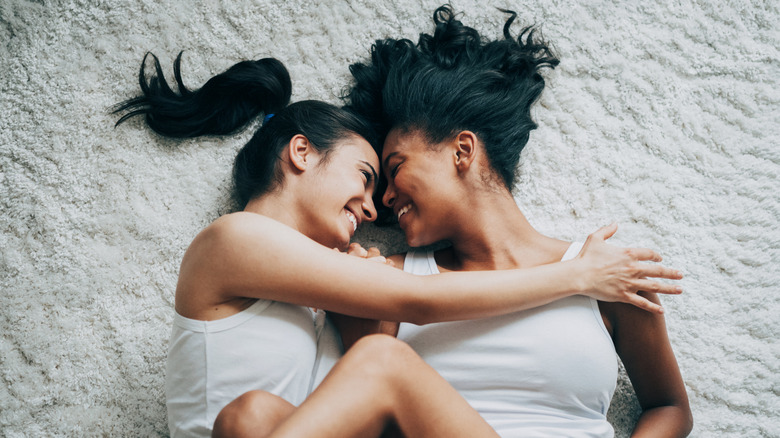 Two women smiling and embracing on a white carpet