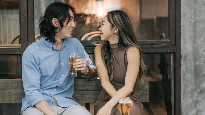 Two smiling people sitting outside drinking beer and talking