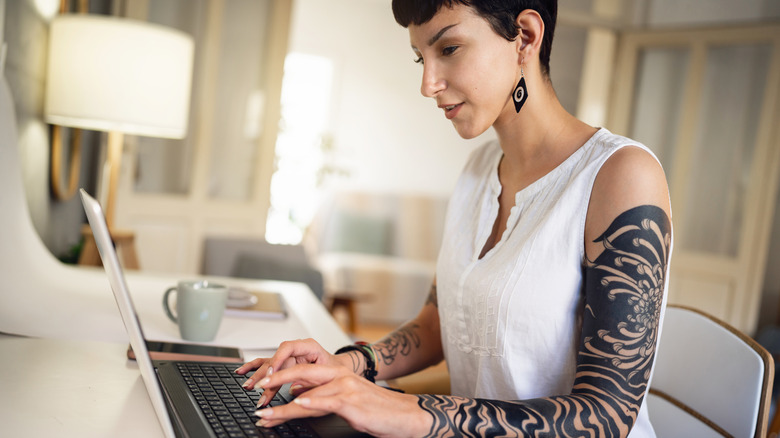 person with tattoo sleeve on laptop