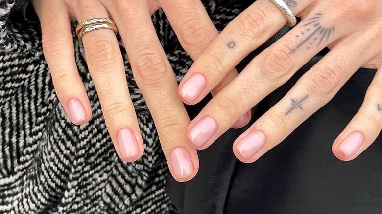 A close-up of two hands with sheer, light-colored nails