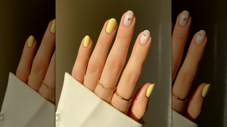 Hand showing combination of yellow nail polish and bee and flower motifs on clear nail polish