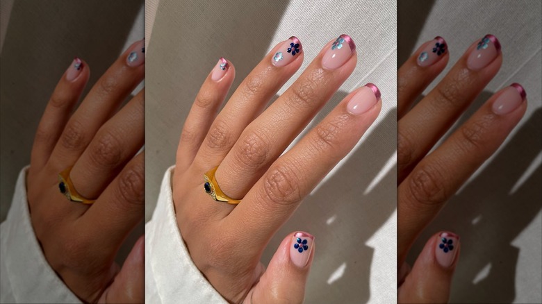 Hand show metallic, pink-tipped manicure accented with blue flowers