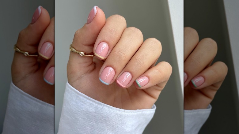 Curled hand showing a square-shaped manicure with pastel-colored tips