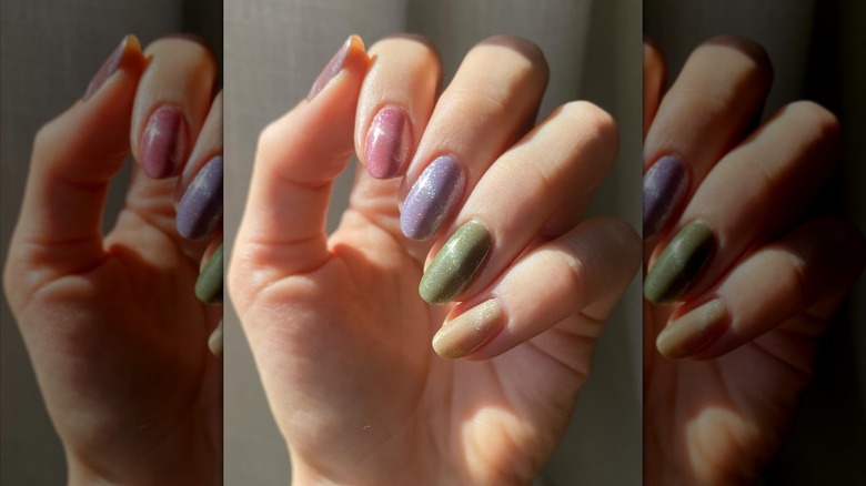 Curled hand showing pink, purple, green, and yellow nail polish with a velvet effect