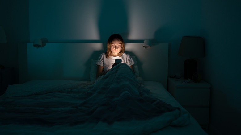 Woman sitting in bed late at night scrolling on phone