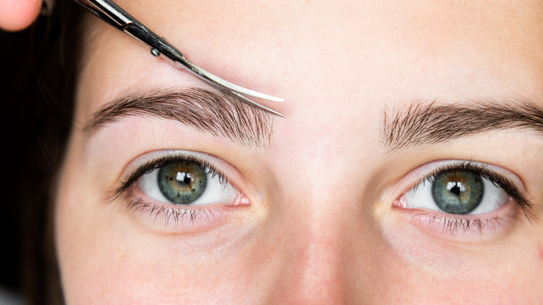 Woman using cuticle scissors to trim eyebrows