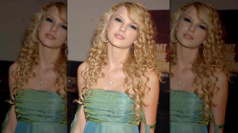 Taylor Swift tilting her head to the side with a curly hairstyle and green dress