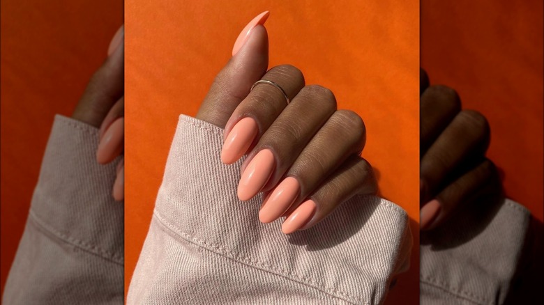 A hand closed around a cream sleeve to show coral nails