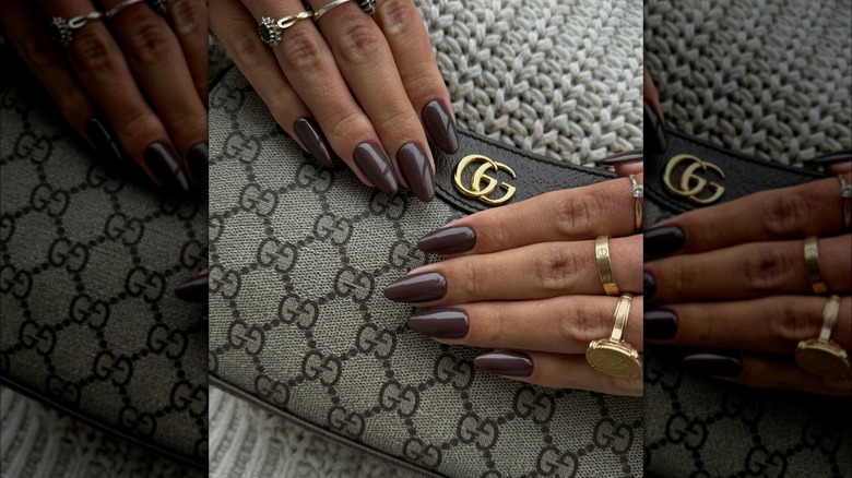 Two hands with mocha brown nails posed against a luxury handbag