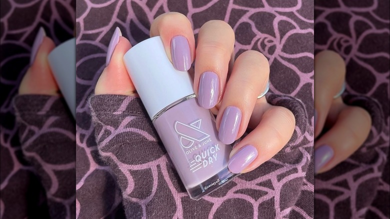 A hand with lavender nails holding a nail polish bottle of the same color