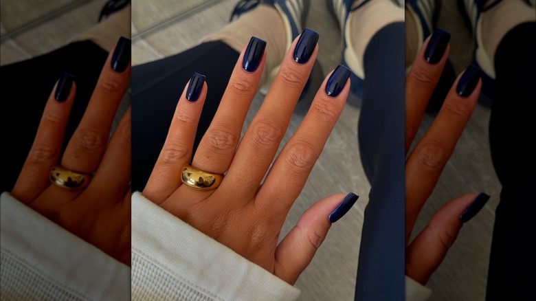 An open hand with navy blue nails featuring blue leggings and tennis shows in the background