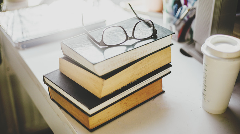 A stack of books on a white table with eyeglasses set on top