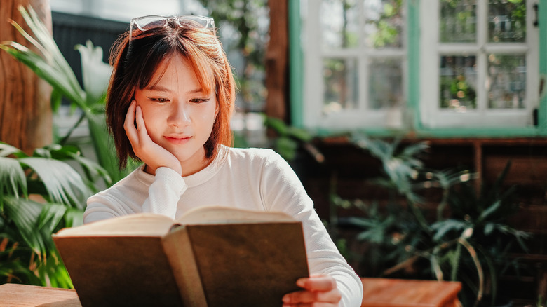 Woman leaning on her hand while reading a book in an outdoor patio setting