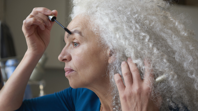 older woman applies eye makeup