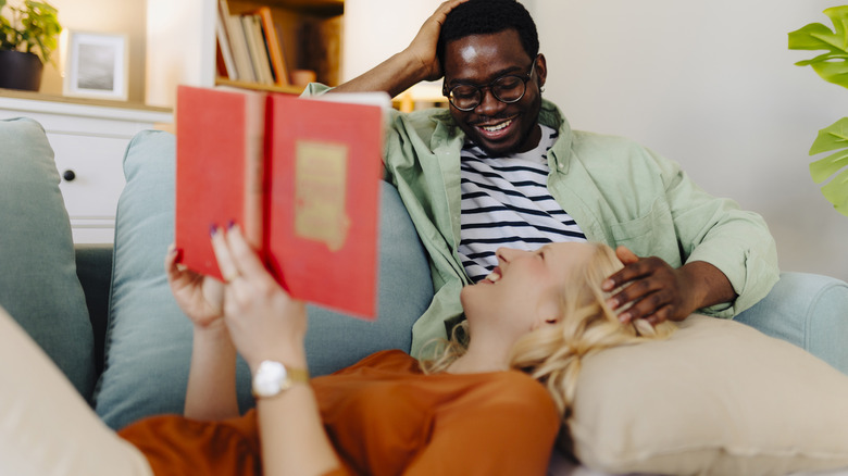 Couple cuddling on the couch, smiling and reading a book