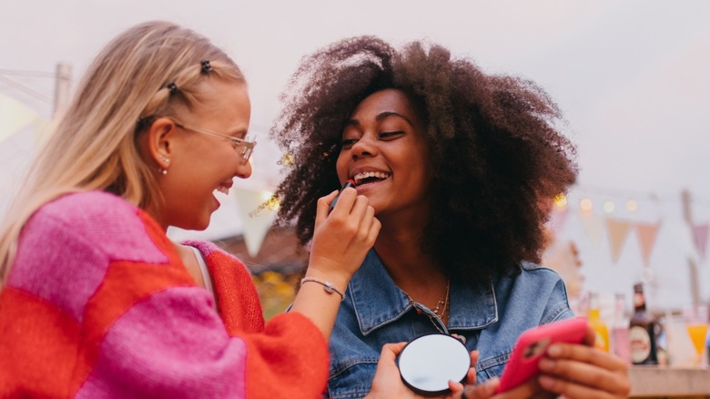 Woman applying lipstick to another woman's lips